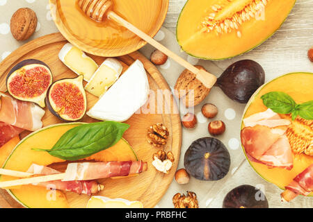 Melone a fette di melone e Prosciutto jamon, le foglie di basilico, fig, Camembert, miele ed essiccato di ciliegio. Antipasto Italiano su sfondo di legno. Foto Stock