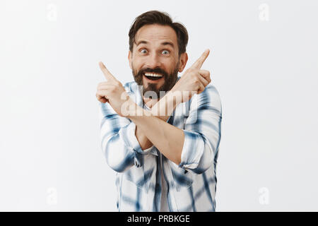 Il miracolo è ovunque. Emozionato funny uomo adulto con la barba e baffi, attraversando bracci sul petto e rivolta verso l'alto in entrambi i lati, sorridente con gioia, in piedi colpiti e soddisfatti oltre il muro grigio Foto Stock