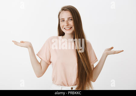 Chi si preoccupa delle conseguenze, chill. Incurante bella ragazza caucasica con lond capelli e lentiggini, sollevando le mani in inconsapevole, clueless espressione, sorridente largamente, non avente alcuna idea e interessi Foto Stock