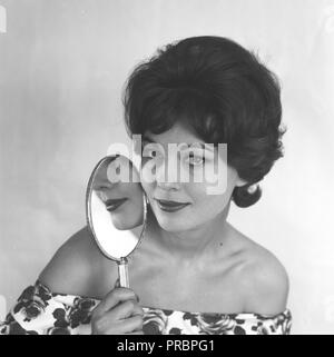 Trucco negli anni cinquanta. Una giovane donna è in possesso di uno specchio per il trucco vicino al suo volto. La Svezia Marzo 1959 Foto Stock