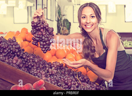 Femmina adulta venditore indossando grembiuli azienda grappolo di uva sul mercato Foto Stock