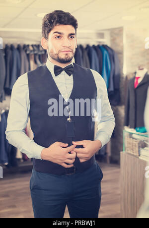 Shopper sta cercando sull'immagine scelta di fronte allo specchio in uomini shop. Foto Stock