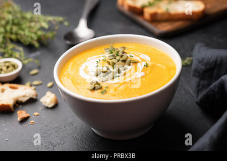 Crema di zucca zuppa nel vaso nero su sfondo di calcestruzzo. Vista ingrandita, il fuoco selettivo. Autunno comfort food concept Foto Stock