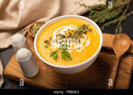 Crema di zucca minestra in ciotola decorata con panna, semi di zucca e timo. Messa a fuoco selettiva Foto Stock