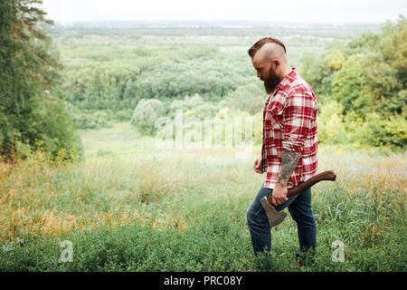 Uomo con ax, barba camicia a scacchi, lumberjack, sullo sfondo della natura passeggiate in foresta Foto Stock