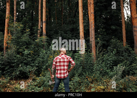 Vista posteriore di lumberjack in foresta tenendo un'ascia sulla sua spalla Foto Stock