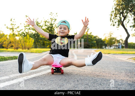 Equitazione per bambini skateboard in estate park. Bambina di imparare a cavalcare skateboard. Active outdoor sport per la scuola e per la scuola materna i bambini. I bambini lo skateboard. Preschooler su longboard. Kid pattinaggio Foto Stock