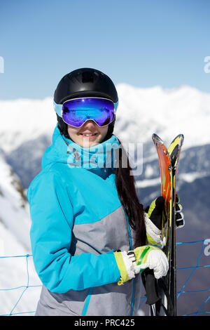 Immagine del giovane sorridente atleta femminile nel casco con gli sci in mano contro il cielo blu Foto Stock