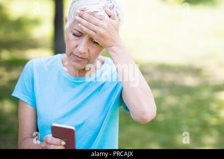 Preoccupato senior donna legge un messaggio su un telefono cellulare nel parco Foto Stock