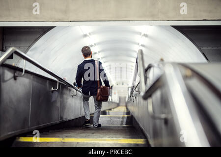 Vista posteriore del hipster imprenditore a piedi giù per le scale in metropolitana, in viaggio per lavoro. Foto Stock