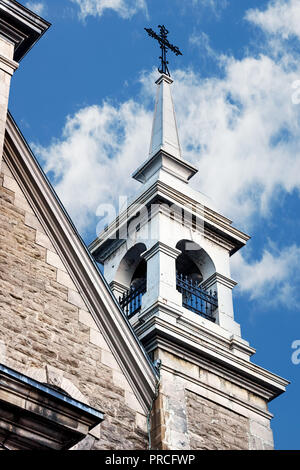 Campanile della chiesa con una croce sulla parte superiore su un luminoso cielo blu e nuvole sullo sfondo Foto Stock