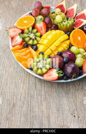 Un assortimento di frutti e bacche platter, fragole mirtilli, mango orange, Apple, uva da tavola, kiwi sul legno grigio Sfondo, spazio copia, verticale Foto Stock