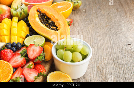 Varietà di frutti, fragole mirtilli, mango orange, pompelmo, banana papaya apple, uva da tavola, kiwi su grigio Sfondo legno, copia spazio per il testo Foto Stock