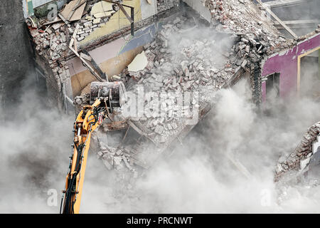 Costruzione di demolizione con un escavatore nella nube di polvere, vista da sopra. Foto Stock