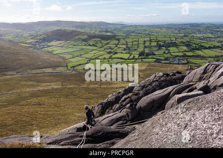 Un esperto rocciatore belaying ai partecipanti dalla sommità di una rupe sulla montagna di gallina nella Mourne Mountains, N.Irlanda. Foto Stock