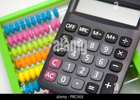 Calcolatrice business e un colorato abacus in background, confronto di due diversi metodi di calcolo. Foto Stock