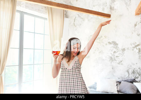 Felice giovane donna ballando con un bicchiere di vino oltre il muro grigio Foto Stock