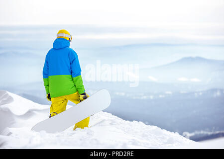 Snowboarder con lo snowboard sorge sulla cima della montagna e guarda per visualizzare Foto Stock