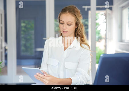 Colpo di giovane assistente finanziario imprenditrice utilizzando la sua tavoletta digitale mentre è seduto in ufficio e di lavoro. Foto Stock