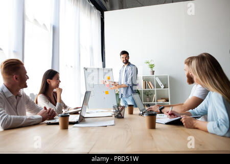 Ottenere migliori risultati insieme. Moderno e giovane uomo a condurre una presentazione aziendale stando in piedi nella sala consiglio. Foto Stock