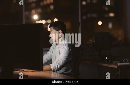 Giovane imprenditore asiatico seduto alla sua workstation a tarda notte Foto Stock