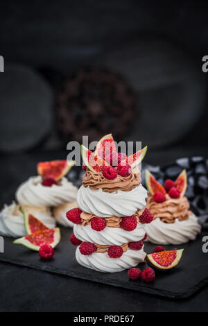 Deliziosa Pavlova meringa decorate torte alla crema di cioccolato, fichi freschi e lamponi su sfondo scuro Foto Stock