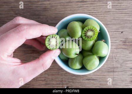 Tagliato a mano hardy kiwi o kiwi berry dal recipiente di ceramica sul tavolo Foto Stock