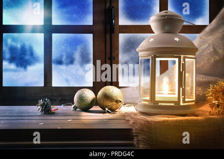 Lampada con decorazione di Natale su un tavolo vicino ad una finestra con sfondo innevato nella notte. Composizione orizzontale Foto Stock