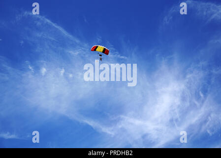 Multicolor red-giallo con paracadute nero tettoia e skydivers contro lo sfondo di una sfocata lighty nuvole e cielo blu. Master in tandem con pass Foto Stock