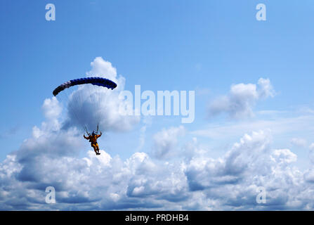Paracadutista sotto un blu scuro poco baldacchino di un paracadute sullo sfondo di un cielo blu e nuvole, close-up. Silhouette del paracadutista con un paracadute Foto Stock