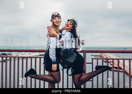 Due college studenti donne di Marine Academy tenendo selfie dal mare indossando uniforme. Happy amici divertendosi sul molo Foto Stock