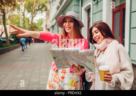 Due donne i turisti alla ricerca di modo giusto usando la mappa di Odessa. Happy amici viaggiatori che mostrano la direzione e ridere Foto Stock