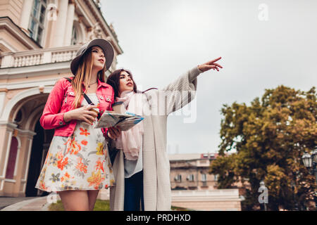 Due donne i turisti alla ricerca di modo giusto usando la mappa di Odessa. Happy amici viaggiatori che mostrano la direzione e ridere Foto Stock