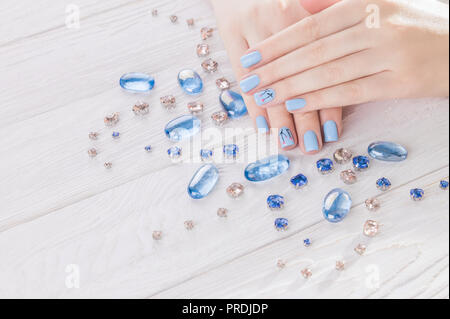 Bella blu manicure circondato con gemme di colore bianco su sfondo di legno Foto Stock