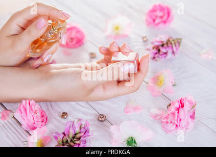Donna applicando profumo sul suo polso circondato con fiori Foto Stock