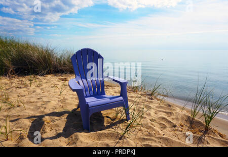 Sedia solitaria sulla spiaggia del lago Michigan. Un viola Chaise Longue su una collina vicino all'acqua. Litorale di Sabbia ed erba verde. Foto Stock