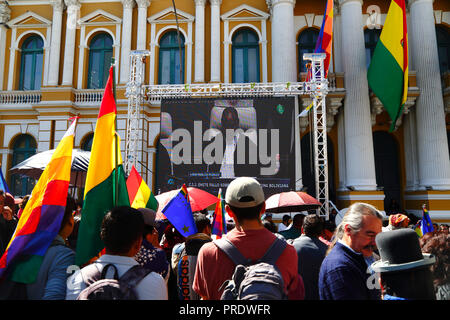 La Paz, Bolivia, 1 ottobre 2018. La gente guarda la sentenza per il caso "obbligo di negoziare l'accesso all'Oceano Pacifico (Bolivia contro Cile)" presso la Corte internazionale di giustizia dell'Aia su uno schermo gigante di fronte all'edificio del Congresso in Plaza Murillo. La Bolivia ha presentato il caso alla CICJ nel 2013; la Bolivia ha perso la sua provincia litoranea verso il Cile durante la guerra del Pacifico (1879-1884) e i negoziati precedenti non hanno compiuto alcun progresso dal punto di vista della Bolivia. Credit: James Brunker/Alamy Live News Foto Stock