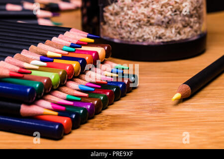 Ordinatamente impilati matite colorate con punti e cicche nel contrastare le righe con un temperamatite su un banco di bambù. Foto Stock