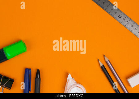 Accessori di cancelleria o scuola merci giacciono su sfondo arancione. Lay piatto. Foto Stock