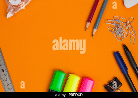 Accessori di cancelleria o scuola merci giacciono su sfondo arancione. Lay piatto. Foto Stock