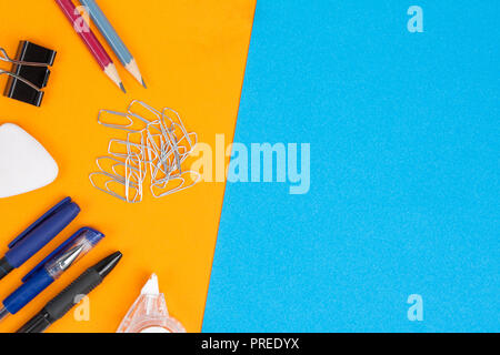 Accessori di cancelleria e scuola merci giacciono su sfondo arancione. Sfondo blu per il testo. Lay piatto. Foto Stock