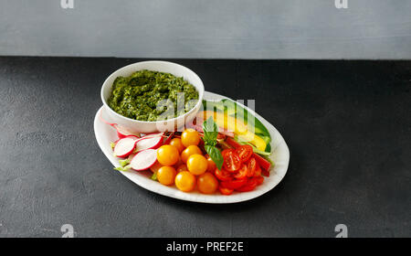 Snack vegetale al pesto servito sulla piastra. Pepe, sedano, rabarbaro, pomodori ciliegini, rafano con pesto Foto Stock