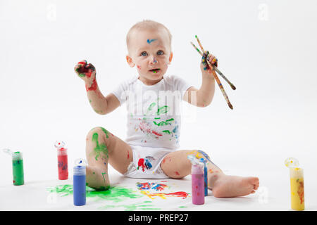 Carino piccolo bambino pittura con pennello e vernici colorate in bianco. Isolato in uno sfondo bianco. Foto Stock