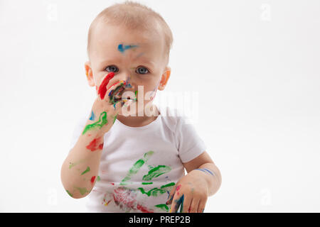 Carino piccolo bambino pittura con pennello e vernici colorate in bianco. Isolato in uno sfondo bianco. Foto Stock