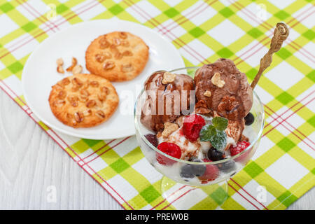 Cioccolato bianco e gelato alla crema con lamponi Ribes e bacche e foglie di menta in un bicchiere sul tovagliolo a scacchi e cookie con i dadi su una piastra Foto Stock