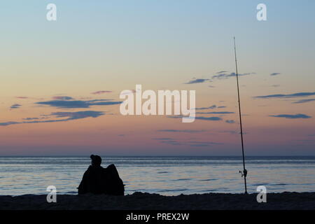 Navigare il pescatore con la canna da pesca sul mar baltico spiaggia al tramonto Foto Stock