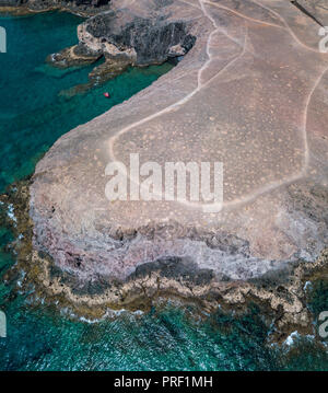 Vista aerea delle coste frastagliate e le spiagge di Lanzarote, Spagna, Canarie. Red dinghy ormeggiata in una baia. Strade e percorsi sterrati. Itinerari a piedi Foto Stock