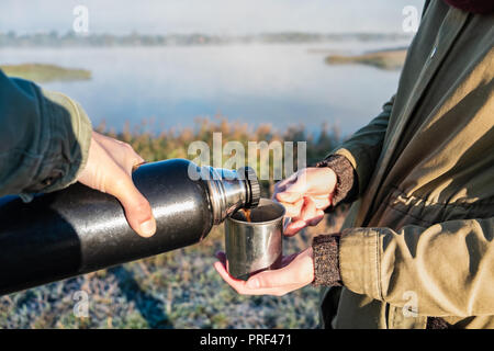 Versare il caffè caldo fuori thermos al bellissimo lungofiume. Due escursionisti godetevi un drink al mattino sulla soleggiata giornata autunnale Foto Stock