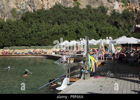 Vouliagmeni Atene Grecia turisti che prendono il sole sul lago Vouliagmeni una Spa naturale - una volta era una caverna, ma il tetto della grotta cadde in seguito all'erosione da t Foto Stock