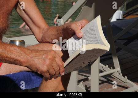 Vouliagmeni Attica Grecia Lago Vouliagmeni ravvicinata di un uomo che legge un libro su una sedia a sdraio Foto Stock